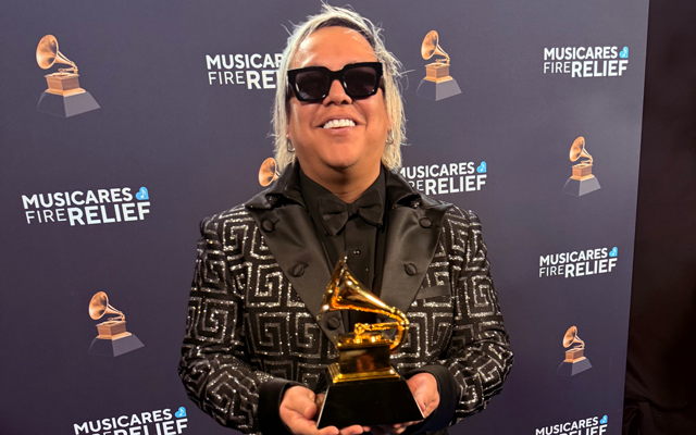 Roger Argenis, sonriente y sosteniendo su Grammy Americano, junto a Lucky Díaz y la Family Jam Band. Un momento inolvidable para este talentoso productor.